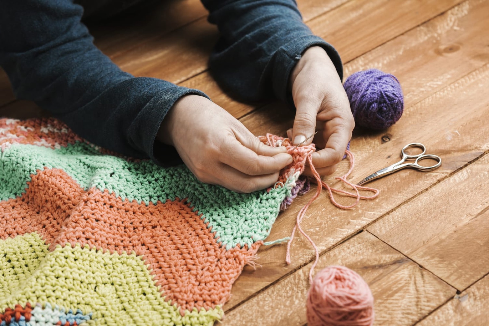 Mãos finalizando uma manta de crochê colorida